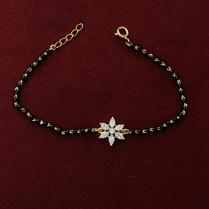 Bracelet with black and gold beads and a silver flower charm on a red background