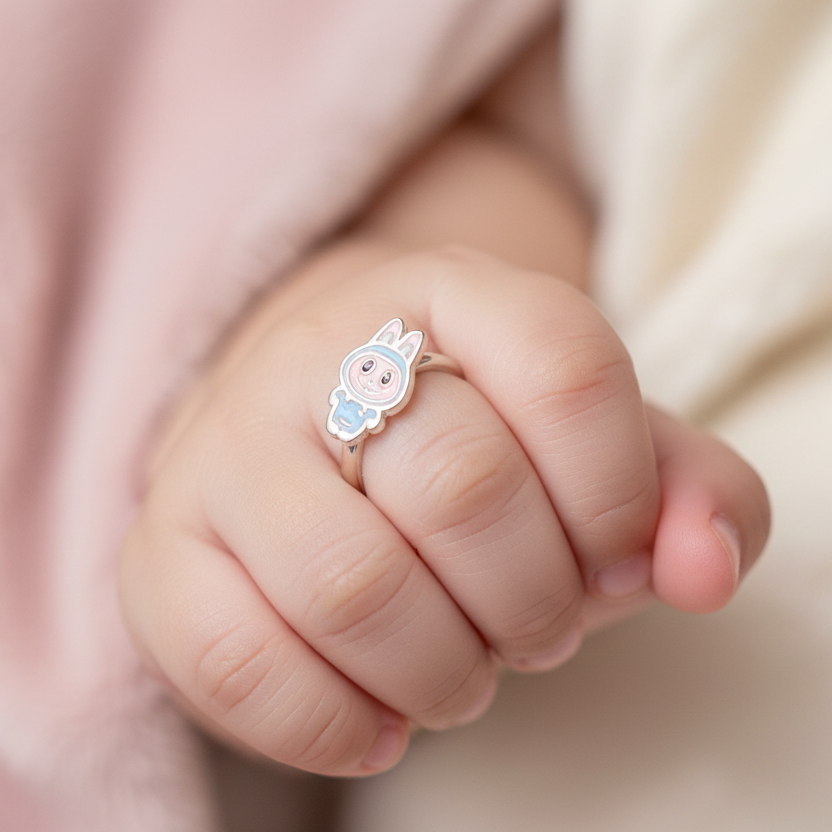 Baby's hand wearing a small ring with a cartoon character on a soft pink background