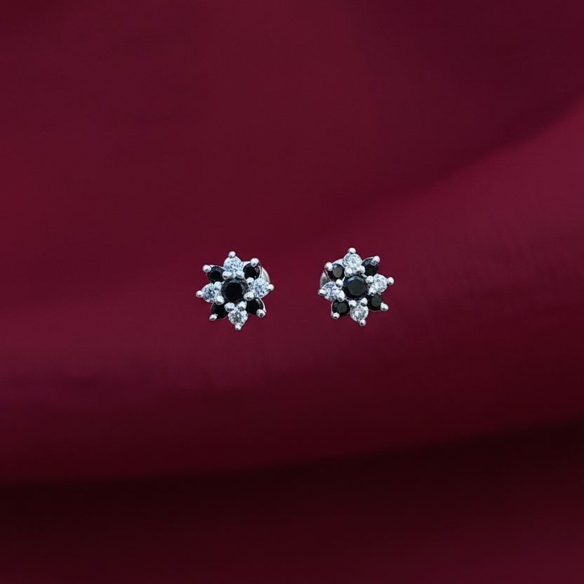 Pair of silver earrings with black stones held between fingers against a red fabric background
