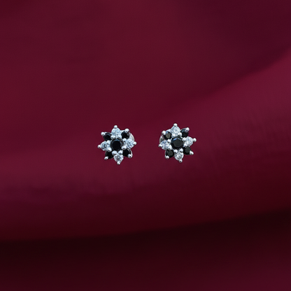 Pair of silver earrings with black stones held between fingers against a red fabric background