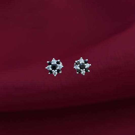 Pair of silver earrings with black stones held between fingers against a red fabric background