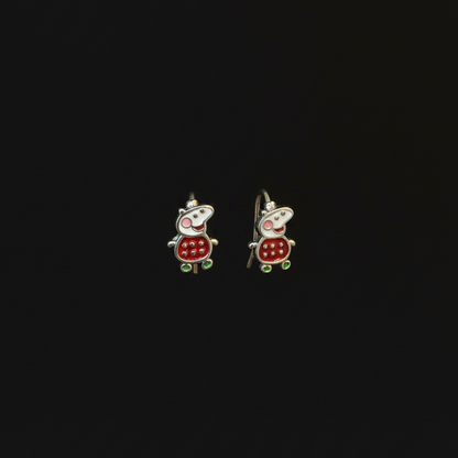 Two small turtle-shaped earrings on a person's finger against a red fabric background