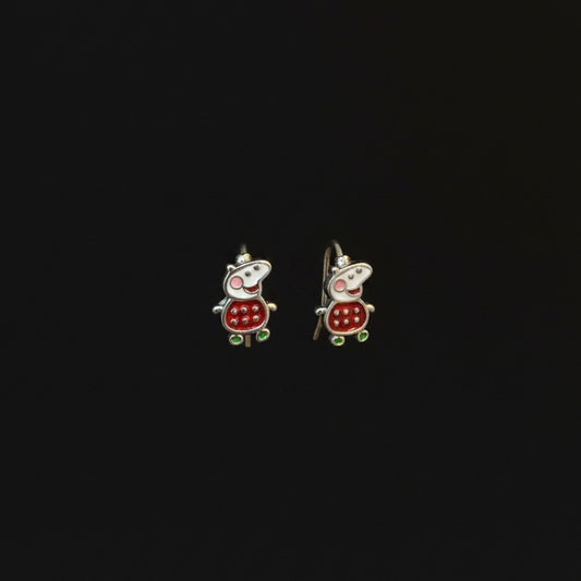 Two small turtle-shaped earrings on a person's finger against a red fabric background