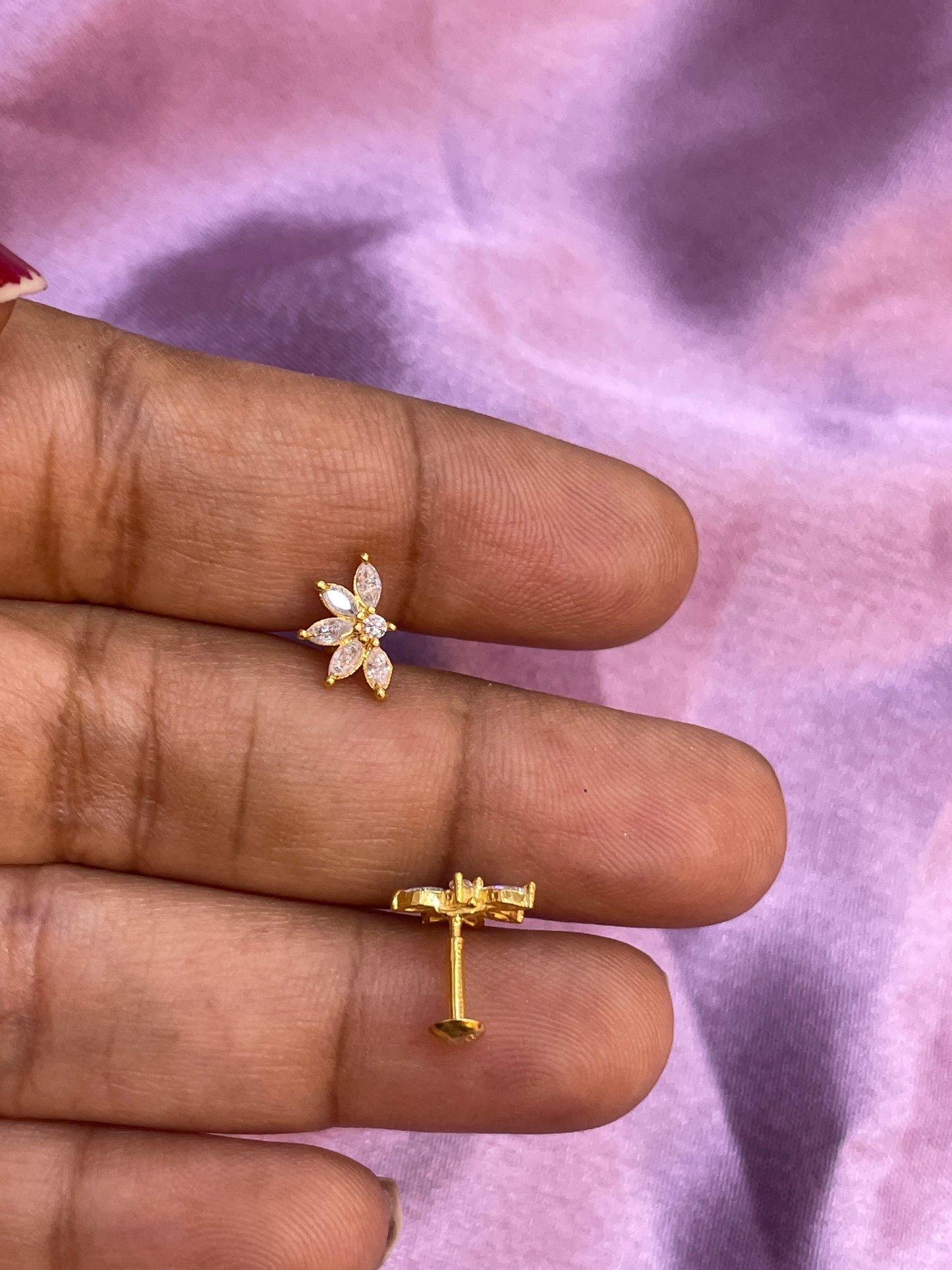 Gold earrings with floral design held between fingers against a purple fabric background