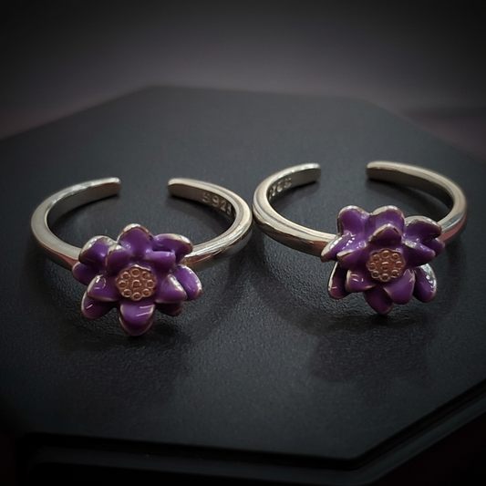 Pair of silver rings with purple flower designs on a black stand against a pink background.