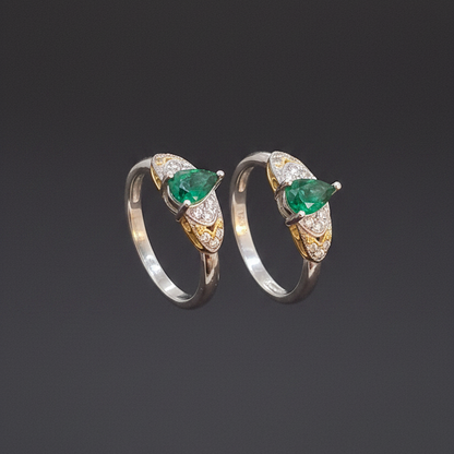 Three emerald and diamond rings on a finger against a pink background