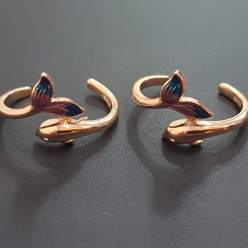 Pair of gold-colored fish tail-shaped earrings on a black stand with a pink background.