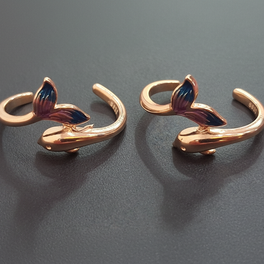 Pair of gold-colored fish tail-shaped earrings on a black stand with a pink background.