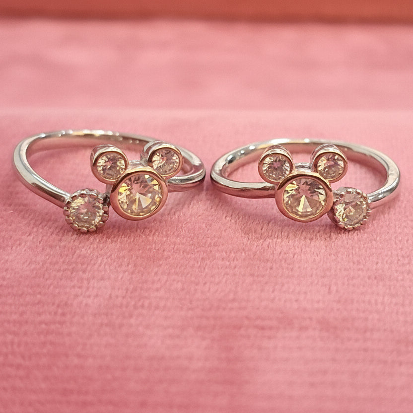 Two gold rings with gemstones on a black stand against a pink background