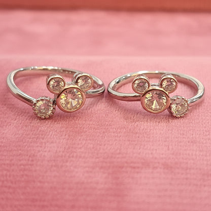 Two gold rings with gemstones on a black stand against a pink background