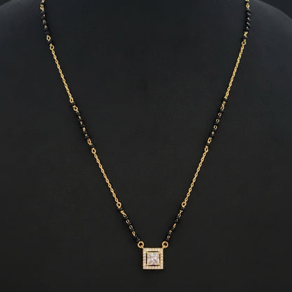 Gold chain necklace with a square pendant on a red fabric background