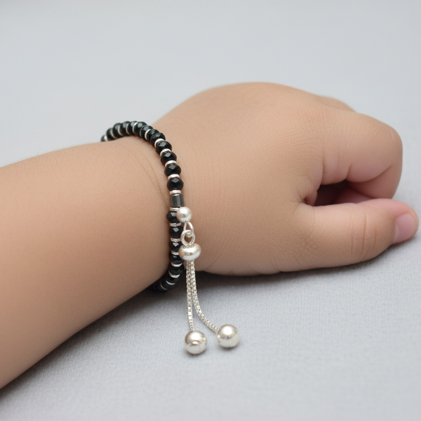Hand wearing a black beaded bracelet with silver charms on a light gray background
