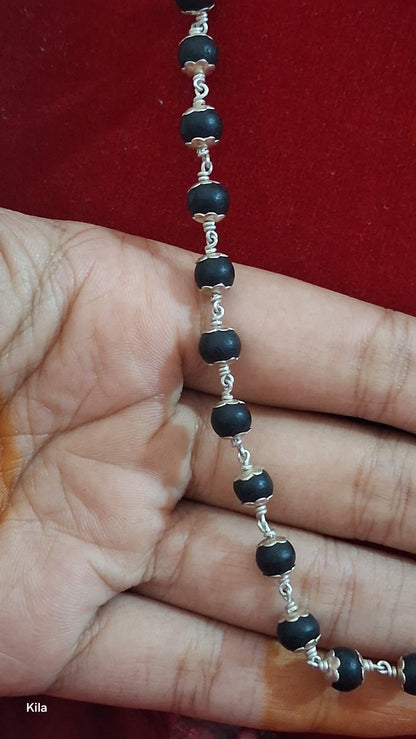 Hand holding a silver necklace with black beads against a red background