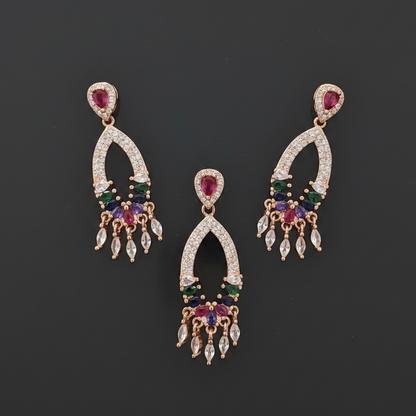 Gold earrings with multicolored gemstones held between fingers against a red fabric background