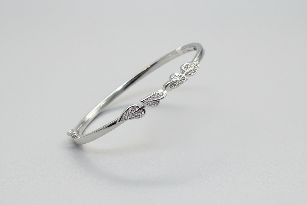 Silver bracelet with leaf designs held in a hand against a red fabric background