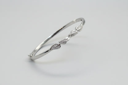 Silver bracelet with leaf designs held in a hand against a red fabric background