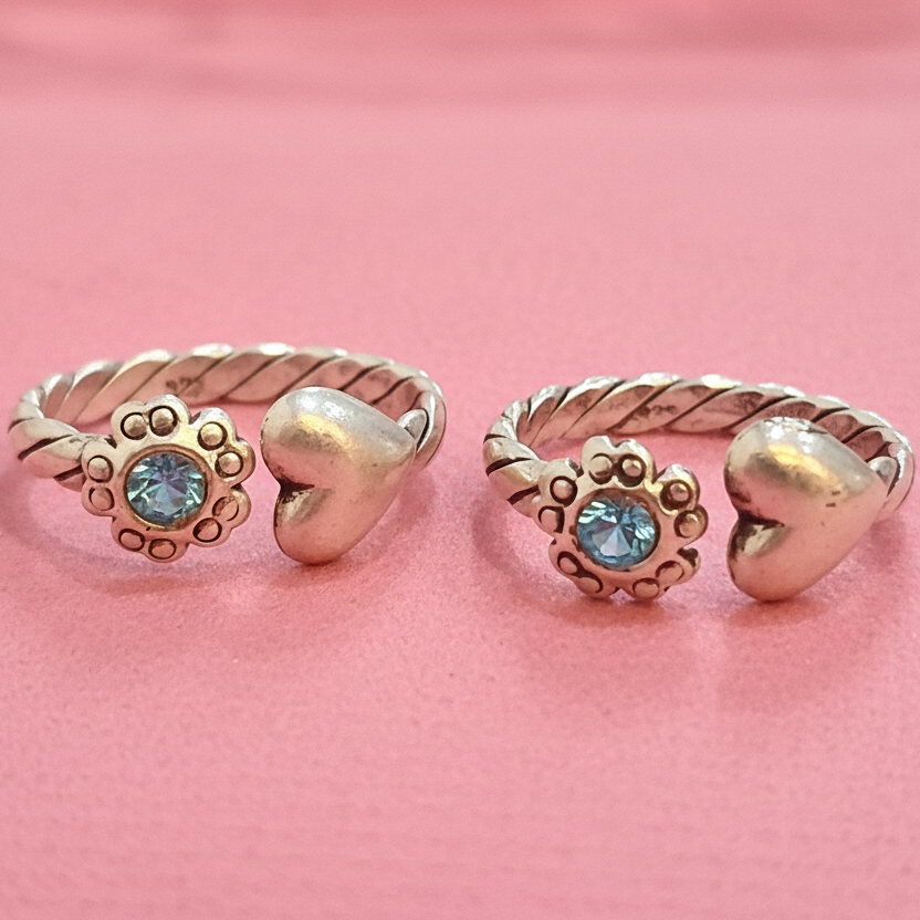 Two gold rings with heart and leaf designs on a pink background