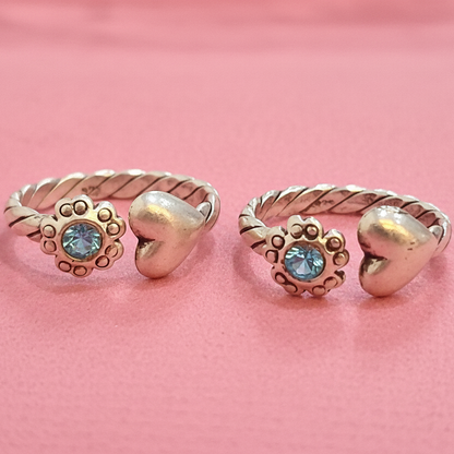 Two gold rings with heart and leaf designs on a pink background