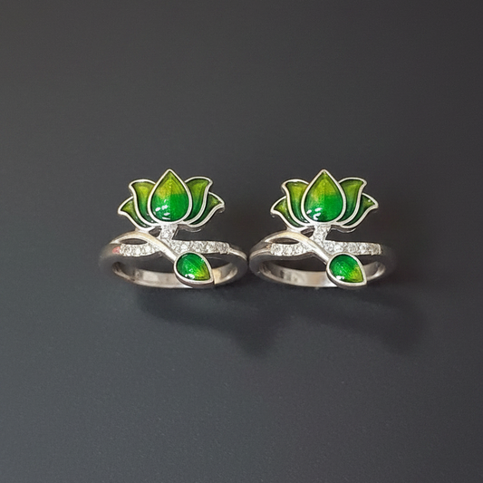 Two silver rings with green gemstones on a finger against a pink background