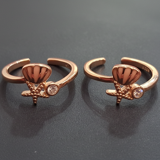 Rose gold hoop earrings with decorative elements on a black stand against a pink background.