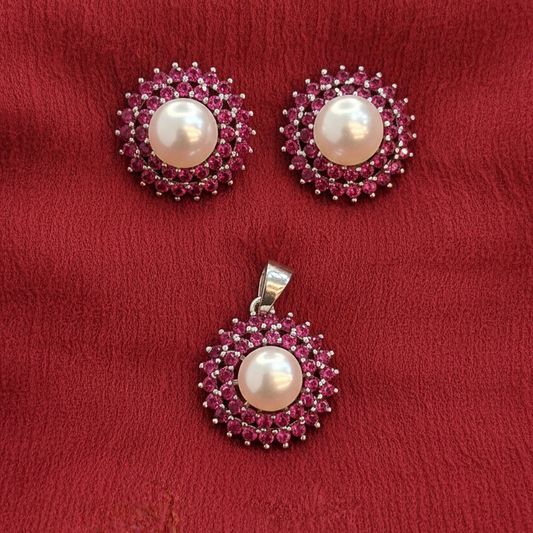 Pearl earrings with pink gemstones on a hand against a red fabric background