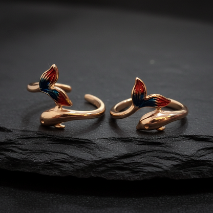 Pair of gold earrings with red and blue accents on a black stand against a pink background.