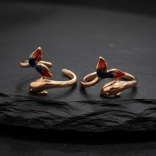 Pair of gold earrings with red and blue accents on a black stand against a pink background.