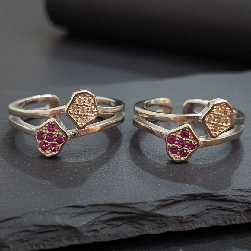 Two gold and silver rings with red gemstones on a black stand against a pink background.