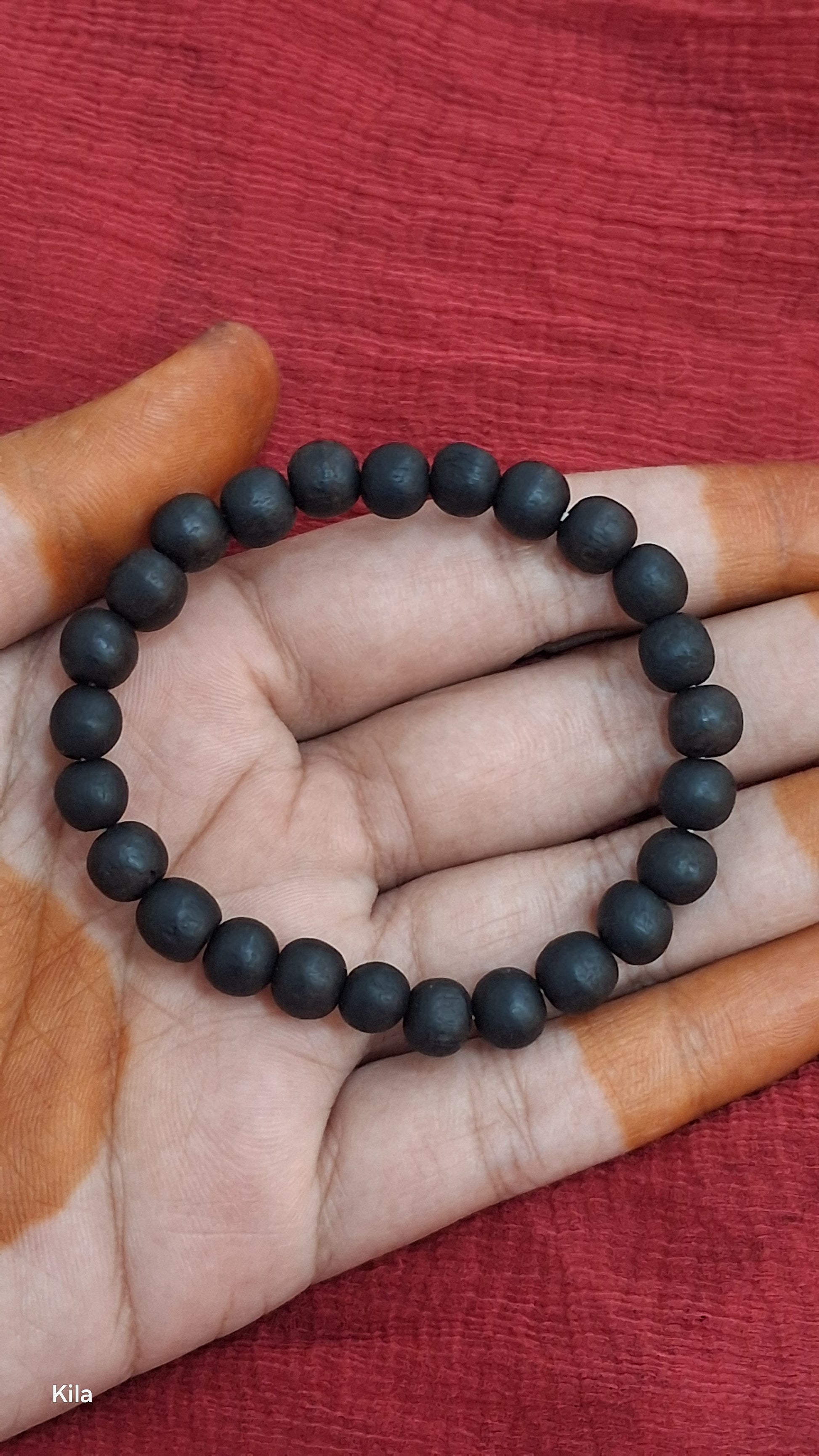 Black beaded bracelet on a hand with a red fabric background