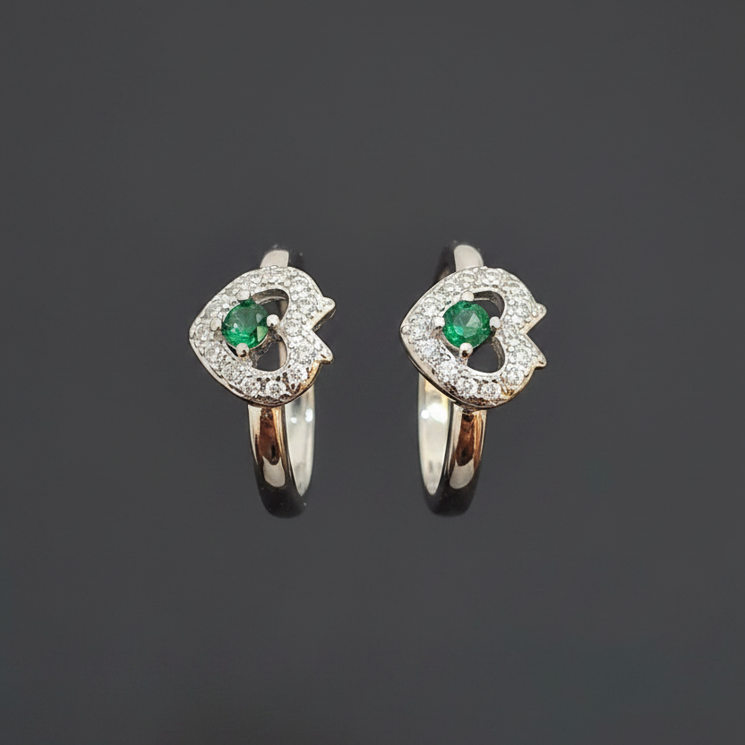 Two heart-shaped rings with green gemstones on a pink background