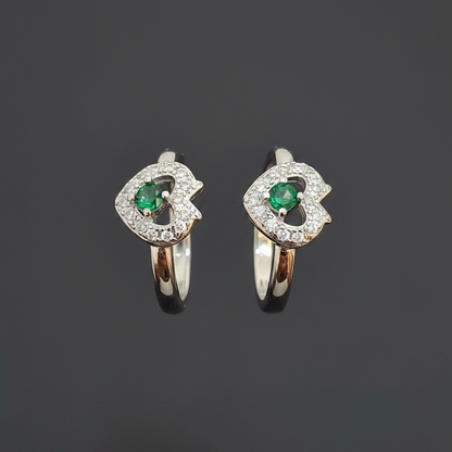 Two heart-shaped rings with green gemstones on a pink background