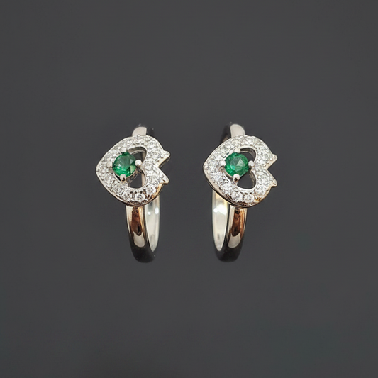 Two heart-shaped rings with green gemstones on a pink background
