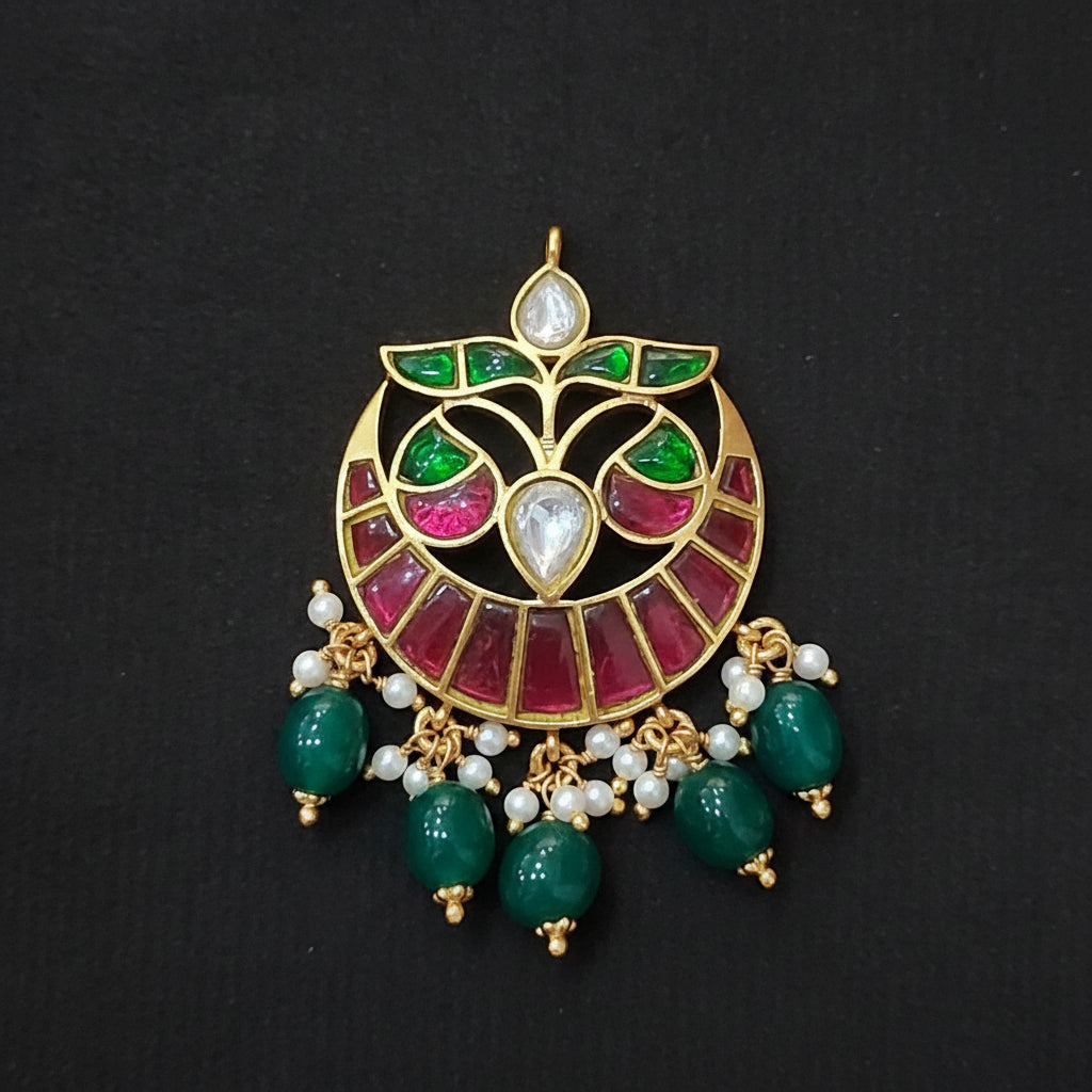 Decorative silver pendant with green and red stones on a maroon background