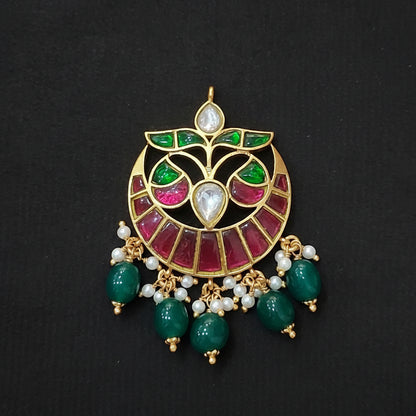 Decorative silver pendant with green and red stones on a maroon background