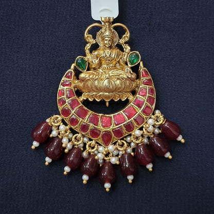 Decorative gold and red pendant with a label on a maroon background