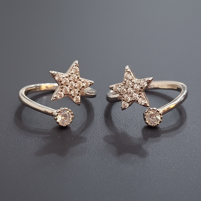 Two gold star-shaped rings on a black stand with a pink background