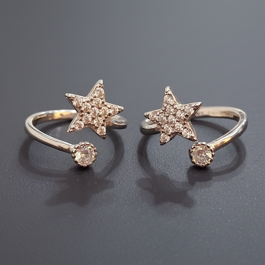 Two gold star-shaped rings on a black stand with a pink background