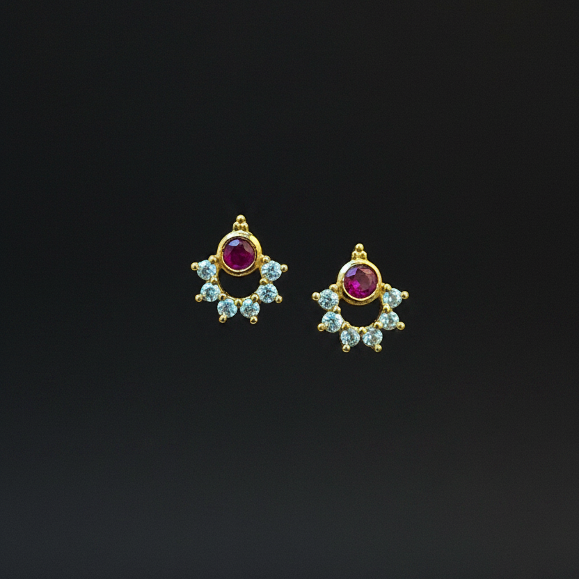 Gold earrings with gemstones on a person's hand against a purple fabric background
