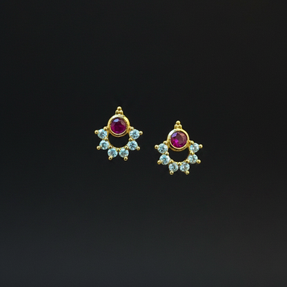 Gold earrings with gemstones on a person's hand against a purple fabric background