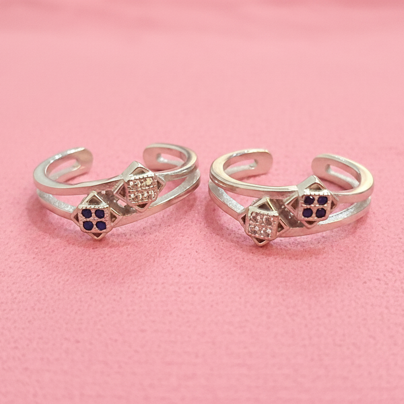 Two gold rings with gemstones on a black stand against a pink background