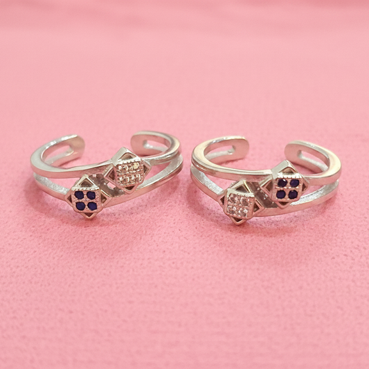 Two gold rings with gemstones on a black stand against a pink background