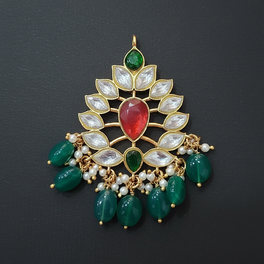 Decorative pendant with green and red stones on a maroon background