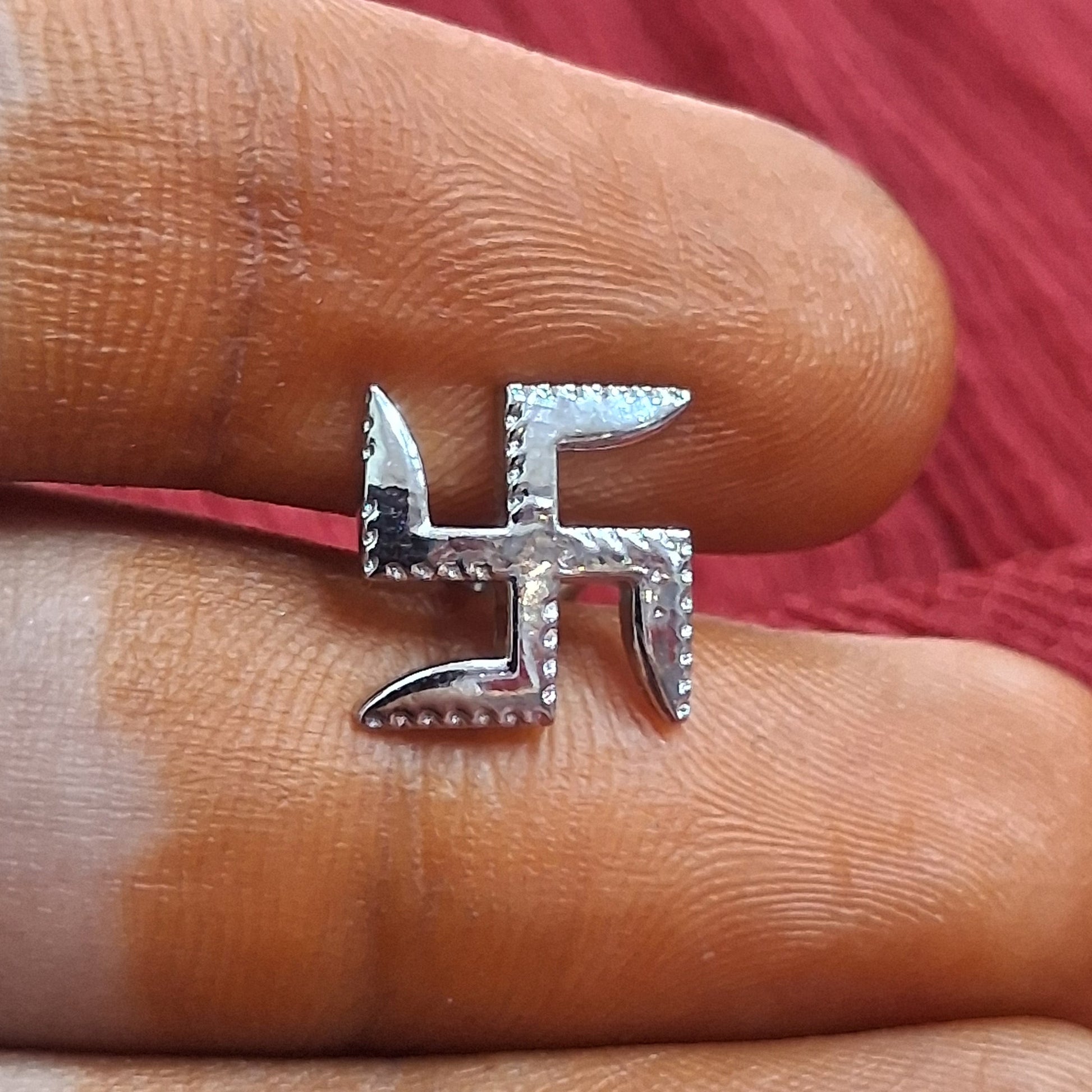 Silver swastika ring on a finger against a red fabric background