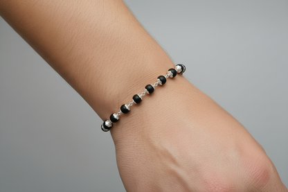Black beaded karungali bracelet with silver clasps on a hand against a red fabric background