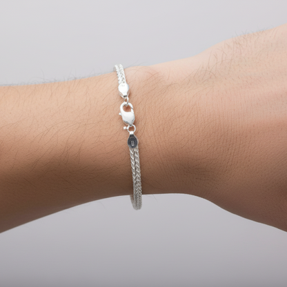 Silver bracelet with a small round charm on a wrist against a gray background