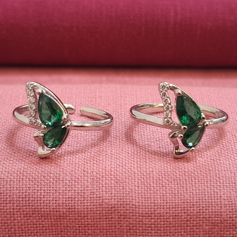 Pair of silver rings with green gemstones on a black stand against a pink background