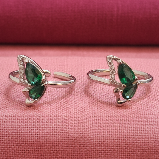 Pair of silver rings with green gemstones on a black stand against a pink background