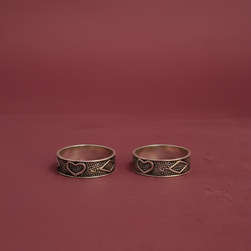 Two silver rings with heart and tribal designs on a finger against a pink background