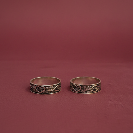 Two silver rings with heart and tribal designs on a finger against a pink background